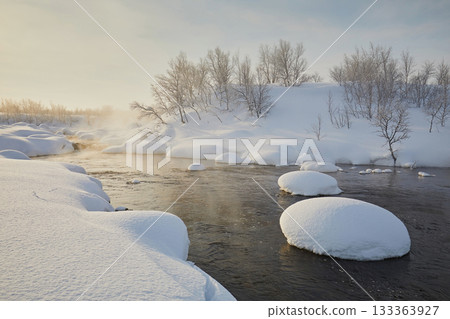 A beautiful freezing river with round drifts and steam against the morning sky. Frosty day, northern winter landscape A beautiful freezing river with round drifts and steam against the morning sky. Frosty day, northern winter landscape 133363927
