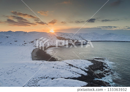 Aerial view of the non-freezing Barents Sea on the Kola Peninsula in winter against the sunset sky and the sun 133363932