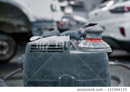 An orbital polisher in a garage shows a close-up of a dusty sander on car bodywork 133364135