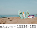 Colorful flip flops with floral accents, sunscreen bottle, and sunglasses on sandy beach, capturing summer vibes and relaxation by the ocean 133364153