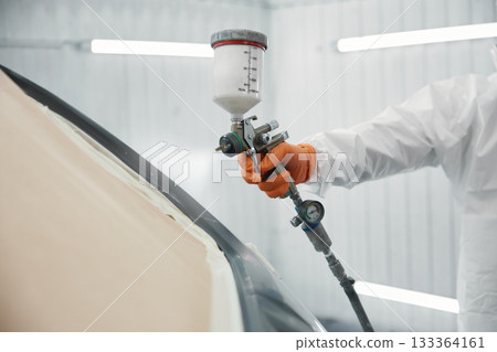 A technician carefully spraying high-quality automotive paint on a car door in a white garage A technician carefully spraying high-quality automotive paint on a car door in a white garage 133364161