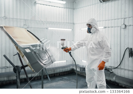 An automotive technician is spray-painting a car panel in a protective paint booth 133364166