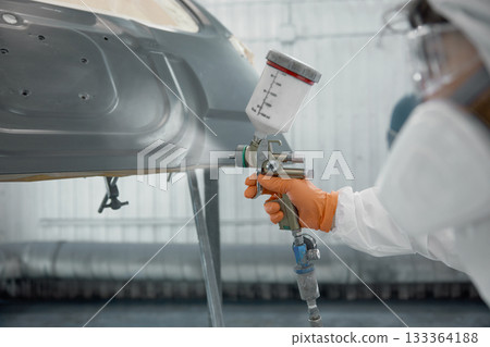 A technician spray-painting car hood inside a controlled automotive spray booth A technician spray-painting car hood inside a controlled automotive spray booth 133364188