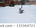 Snow Covered Park Bench in Quiet Winter Scene with Buildings in Background 133364721