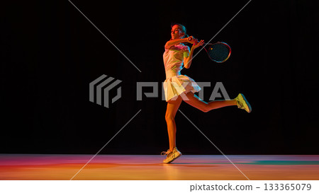 Young tennis player illuminated by vivid lights during energetic backhand motion Young tennis player illuminated by vivid lights during energetic backhand motion 133365079