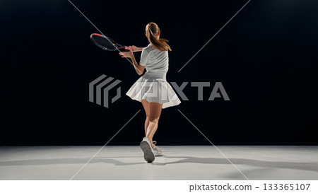Teenage girl tennis player finishing swing with focus and determination 133365107