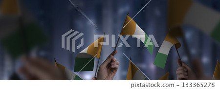 Cote dIvoire flags in their hands on a blurred urban background 133365278