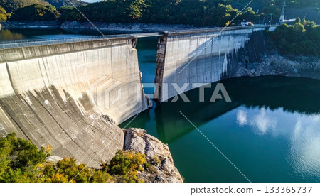 Nature landscape view of a concrete dam on the river, featuring a bridge and blue sky with clouds Nature landscape view of a concrete dam on the river, featuring a bridge and blue sky with clouds 133365737
