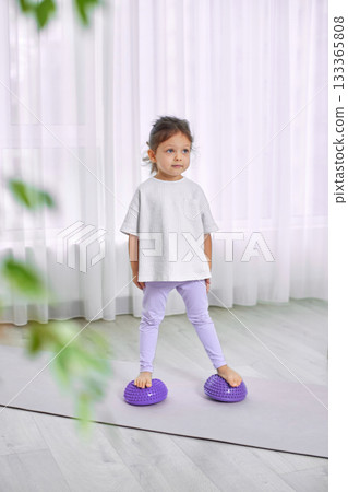Young girl balancing on purple sensory pods on a yoga mat at home Young girl balancing on purple sensory pods on a yoga mat at home 133365808