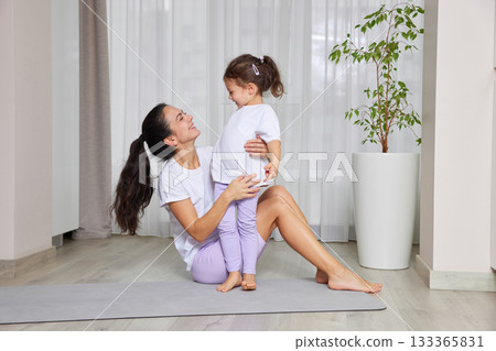 Mother and daughter smiling while exercising and playing on a yoga mat 133365831