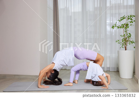 Mother and daughter exercising in a bridge pose on a mat at home 133365832