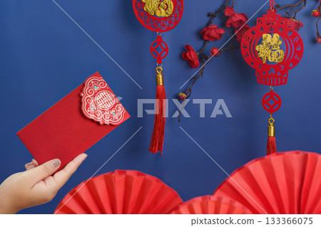 Lunar New Year celebration. Hand holding red envelope with traditional decorations. 133366075