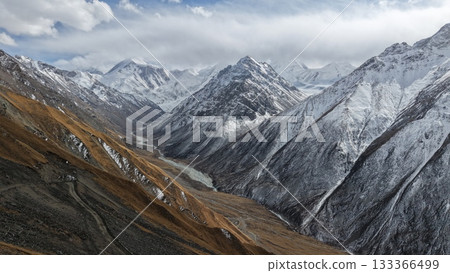 Majestic snow-capped mountains with valley and river under cloudy sky 133366499