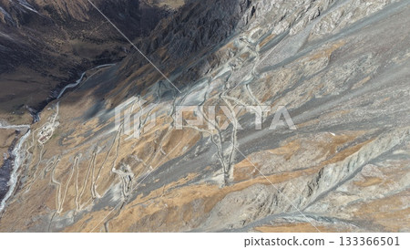 Aerial view of winding mountain road through rocky terrain and valleys Aerial view of winding mountain road through rocky terrain and valleys 133366501