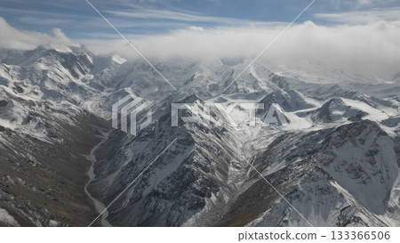 Snow-covered mountain range with dramatic peaks and valleys under clouds Snow-covered mountain range with dramatic peaks and valleys under clouds 133366506