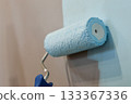 A renovator is seen painting an apartment wall with a roller tool, carefully covering the entire surface with white paint to refresh and renew the room's appearance 133367336