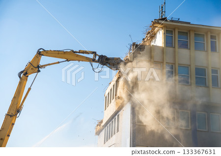 Powerful demolition of a concrete office building with a yellow high-reach excavator. Concept of transformation, destruction and construction renewal. Powerful demolition of a concrete office building with a yellow high-reach excavator. Concept of transformation, destruction and construction renewal. 133367631