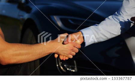 Male hand giving key of car to buyer of electric automobile outdoor. Handshake between salesman and new owner of modern auto after successful deal. Concept of buy or rent car. Slow mo 133367787