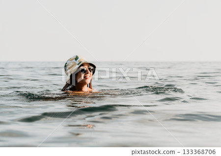 Woman Swimming Ocean Sunglasses Hat - A woman in sunglasses and a hat swims in the ocean. Woman Swimming Ocean Sunglasses Hat - A woman in sunglasses and a hat swims in the ocean. 133368706