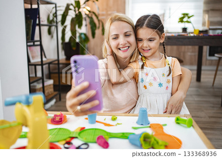 Mother and daughter take a cheerful selfie while playing with colorful plasticine 133368936