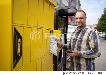 Delivery man retrieving package from yellow locker in urban setting during daylight 133369008