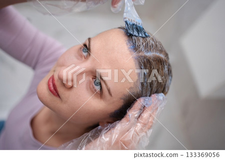 Hairdresser applying hair dye to woman with brush in salon Hairdresser applying hair dye to woman with brush in salon 133369056