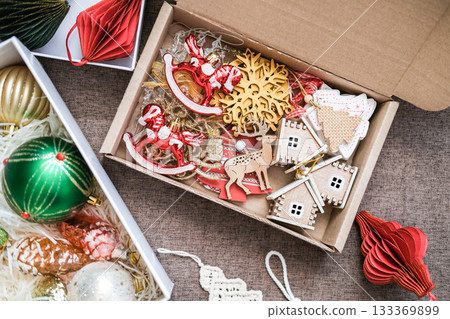 Cardboard box filled with rustic wooden Christmas decorations: rocking horses, snowflake, houses and deer next to box of glass balls. Storing Christmas tree decorations, tree decorating, natural style Cardboard box filled with rustic wooden Christmas decorations: rocking horses, snowflake, houses and deer next to box of glass balls. Storing Christmas tree decorations, tree decorating, natural style 133369899