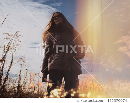 A confident white woman walking in a field at sunset, captured in a cinematic nostalgic film aesthetic. Slow-living vibes, outdoor lifestyle theme. A confident white woman walking in a field at sunset, captured in a cinematic nostalgic film aesthetic. Slow-living vibes, outdoor lifestyle theme. 133370074