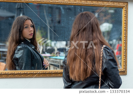 A young, positive  woman makes various grimaces and enjoys her reflection in the mirror 133370334