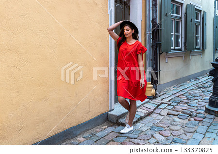 a young sensual woman in a red dress and a black hat on a cobbled old town street 133370825