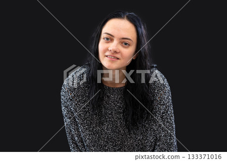 portrait of young woman with long dark hair wearing gray knitted sweater over black background 133371016