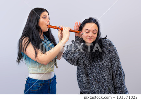 two attractive teenager girls having fun with wooden flute isolated on light background 133371022