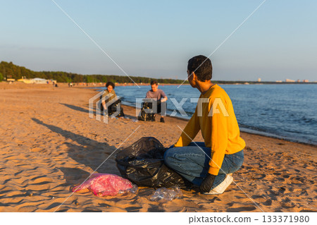 Earth day. Volunteers activists team collects garbage cleaning of beach coastal zone. Woman mans puts plastic trash in garbage bag on ocean shore. Environmental conservation coastal zone cleaning 133371980