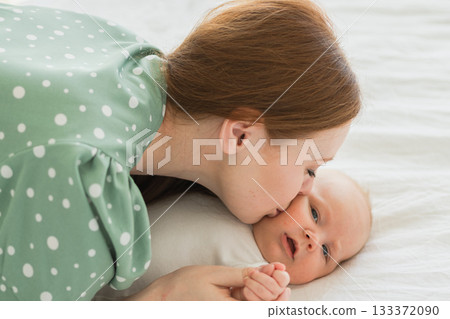 Happy family at home. Mother playing with little toddler child on bed. Mom baby relax playing having fun together. Mother looks at baby with love care. Mom of breast feeding baby rest in living room 133372090