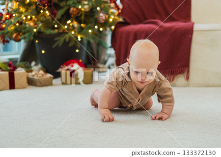 Merry Christmas Xmas. Happy newborn baby child crawling near Christmas tree in living room at home. Little girl kid smiling in room with Christmas decorations. Happy baby in first Christmas eve 133372130