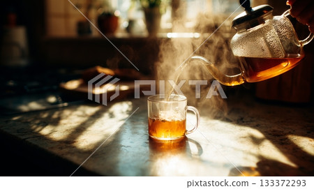 Warm tea being poured into a glass cup on a sunny kitchen countertop 133372293