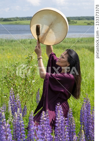 Female shaman drumming among the flowers 133373378