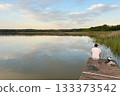 Fishermen catch fish from a wooden pier at sunset over a calm lake 133373542