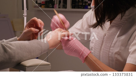 Modern manicure. Gel polish. Beauty technician nail hands in pink gloves using emery board on fingernails care female routine cosmetic treatment. 133373831