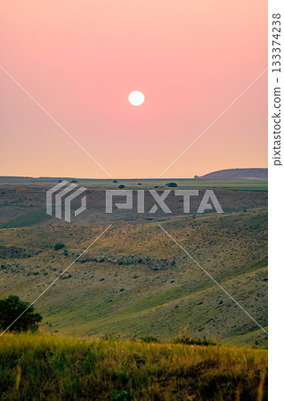 The sun sets over rolling steppe hills, painting the sky in soft orange hues The sun sets over rolling steppe hills, painting the sky in soft orange hues 133374238