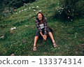 enthusiastic woman with plaid shirt relaxing barefoot amidst bright sunlight in wide open meadow 133374314