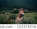 pensive white woman, quietly thoughtful woman resting on rocky terrain in tranquil mountain setting 133374318