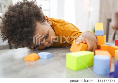 Child with curly hair plays with colorful blocks indoors Child with curly hair plays with colorful blocks indoors 133377173