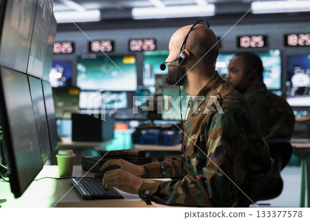 Military dispatcher in command post ready to respond to emergencies and communicate with soldiers on front lines. Middle Eastern war telecommunications operator in uniform talking in headset mic Military dispatcher in command post ready to respond to emergencies and communicate with soldiers on front lines. Middle Eastern war telecommunications operator in uniform talking in headset mic 133377578