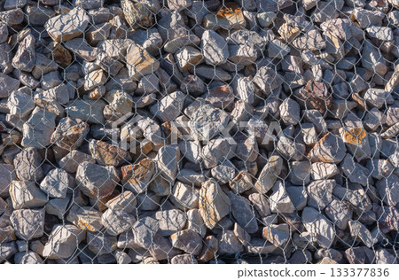 Gabion stone wall construction close up. New stone fence in wire grid, iron cage with rocks 133377836