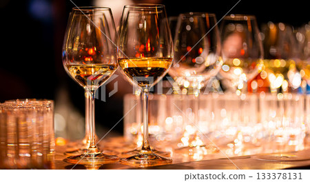 Elegant scene of wine being poured into glasses aligned in a row, showcasing the rich colors and graceful flow of the liquid, set against a dark, warm background, ideal sophisticated dining settings Elegant scene of wine being poured into glasses aligned in a row, showcasing the rich colors and graceful flow of the liquid, set against a dark, warm background, ideal sophisticated dining settings 133378131