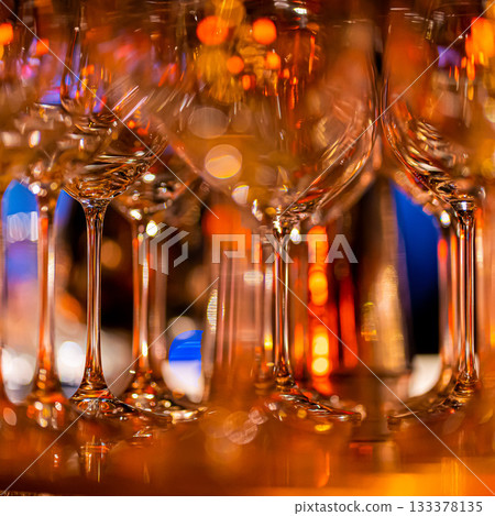 Elegant scene of wine being poured into glasses aligned in a row, showcasing the rich colors and graceful flow of the liquid, set against a dark, warm background, ideal sophisticated dining settings 133378135