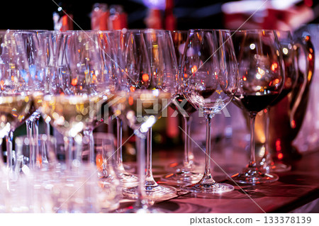 Elegant scene of wine being poured into glasses aligned in a row, showcasing the rich colors and graceful flow of the liquid, set against a dark, warm background, ideal sophisticated dining settings Elegant scene of wine being poured into glasses aligned in a row, showcasing the rich colors and graceful flow of the liquid, set against a dark, warm background, ideal sophisticated dining settings 133378139
