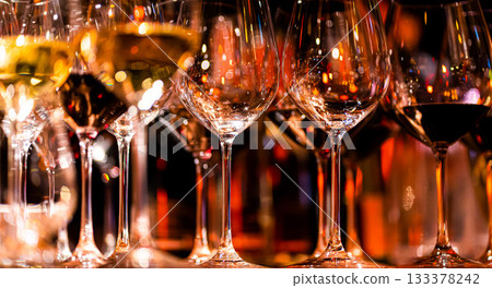 Elegant scene of wine being poured into glasses aligned in a row, showcasing the rich colors and graceful flow of the liquid, set against a dark, warm background, ideal sophisticated dining settings 133378242