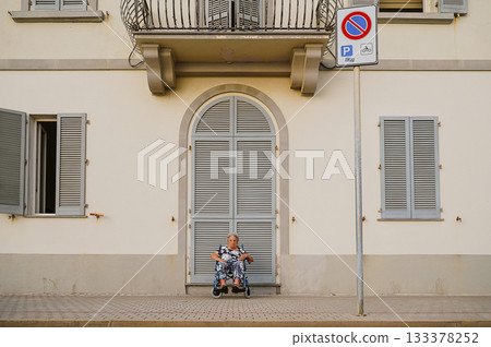 Elderly Woman Relaxing in Wheelchair by Building Elderly Woman Relaxing in Wheelchair by Building 133378252